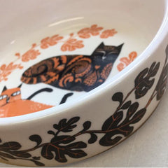 Lush Designs cat feeding bowl pictured from the side showing a glimpse of two orange and black cats, the sides of the bowl decorated with fig leaves 