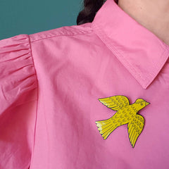 Lush designs yellow bird-shaped badge pin worn on a strawberry pink blouse