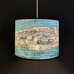Lush Designs lampshade with print of a coastal village and the sea and sky in shades of blue