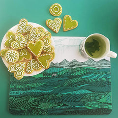 Mat printed with green landscape with green iced biscuits and cup of green tea