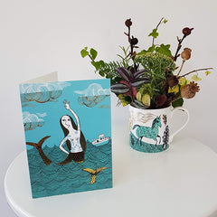 Mermaid birthday card next to a unicorn mug containing an autumn posy
