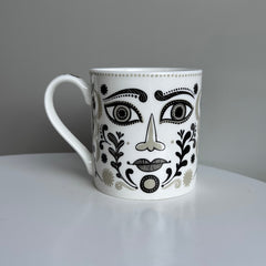 White mug with black and gray face design on a gray background