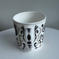 White mug with black and gray floral pattern on a white surface with gray background