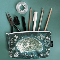 Pencil case with hedgehog design containing stationery items on a green background