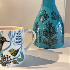 Ceramic mug with bird design and blue lamp base with leaf pattern on a light background