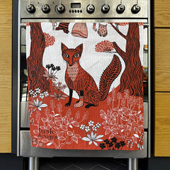 Stainless steel oven with a decorative towel featuring a fox design on a wooden kitchen background