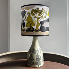 Table lamp with decorative shade featuring a design of a person, tree, and animal on a neutral background.