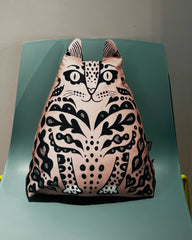 A pink cat-shaped backpack with a black and white patterned design, resting on a mint green chair.