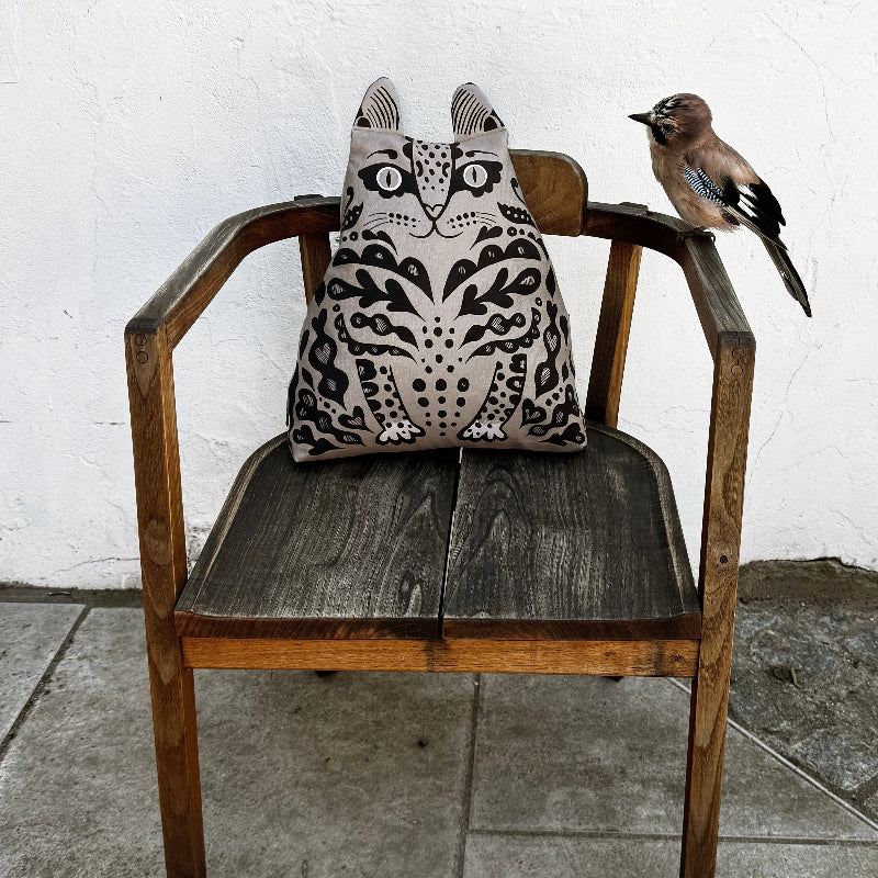 Wooden chair with a decorative pillow featuring a cat design and a bird perched on it.
