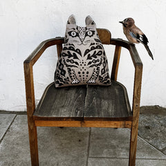 Wooden chair with a decorative pillow featuring a cat design and a bird perched on it.