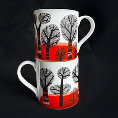 Two stacked white ceramic mugs with black tree silhouettes and a bright red landscape design, set against a solid black background.