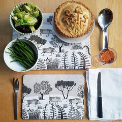 Table setting of wild boar table mats with a mushroom pie, glass of wine and vegetables