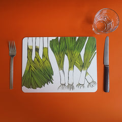 Table mat printed with leeks on an orange table set with fork, knife and glass