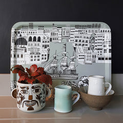 Tray with graphic print of a sailing ship on the river thames, with a funny face plant pot, red plant and two little jugs 