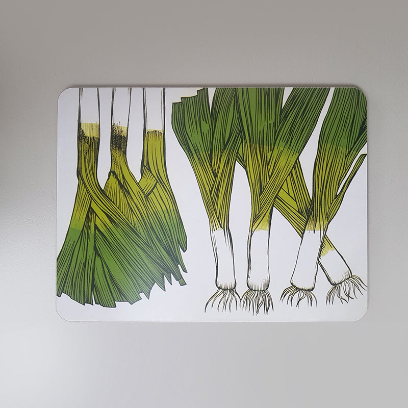 Table mat printed with leeks on an orange table set with fork, knife and glass