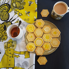 Lush Designs Bee Keeper print tea towel with some hexagonal iced biscuits, tea and honey