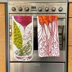 vegetable print oven gloves and carrot print tea towel hanging on an oven door
