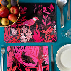 Bird print mats in pinks, reds and black on a blue tablecloth with fruit