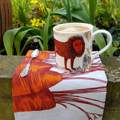 Lion mug photographed in the garden with a carrot printed tea towel