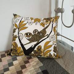 Lush designs cushion with print of slender loris on a bed with a grey patchwork quilt